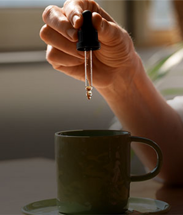 Person adding CBD & THC tinctures and softgels to coffee, symbolizing relaxation.